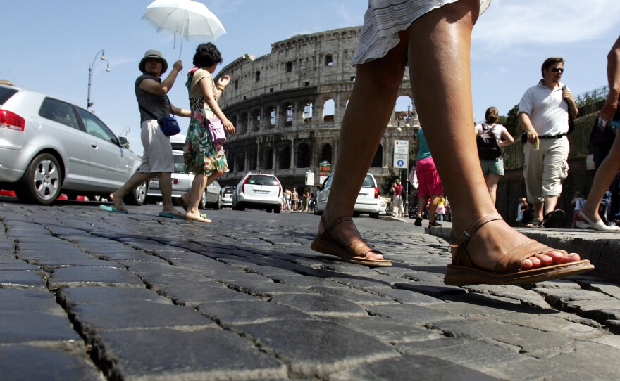 Pedestrians cross the cobblestoned Via dei Fori Imperiali in front of Rome's Colosseum.