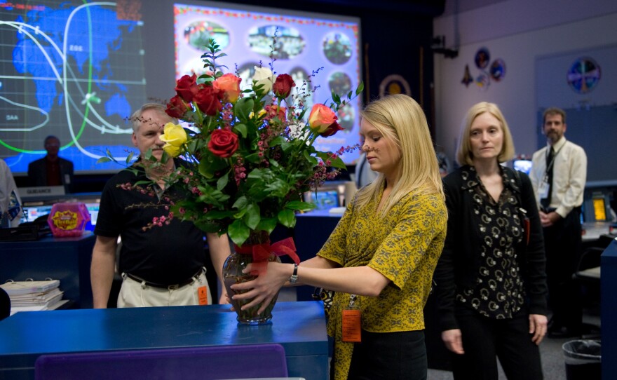 MacKenzie Shelton (center) sets up a bouquet of flowers commemorating the 100th mission they'd sent flowers to the Mission Control Center in 2009. Her parents, Mark (left) and Terry (right), look on.