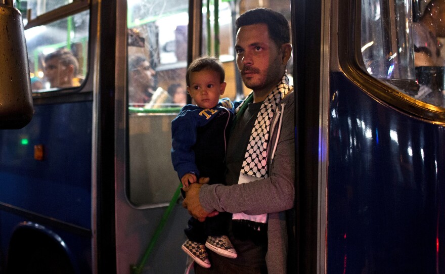 A man and a child stand next to the door of a bus provided by Hungarian authorities for migrants and refugees stranded at the Keleti train station in Budapest, Hungary, on Sept. 5, 2015. The migrants boarded buses provided by Hungary's government and headed to Austria, which allowed them in.