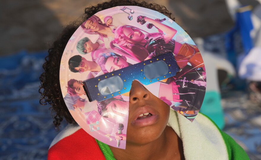 A beachgoer wearing special eclipse glasses looks up during the beginning phase of a solar eclipse at Puerto de Sagunto beach near Valencia, Spain, Wednesday, Aug. 12, 2026.