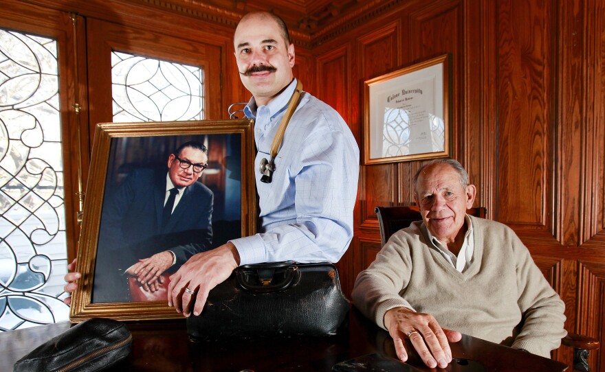 Michael Sawyer, the latest doctor in his family, holds a portrait of his grandfather Dr. Ken Sawyer, while his father Robert, a surgeon, looks on.