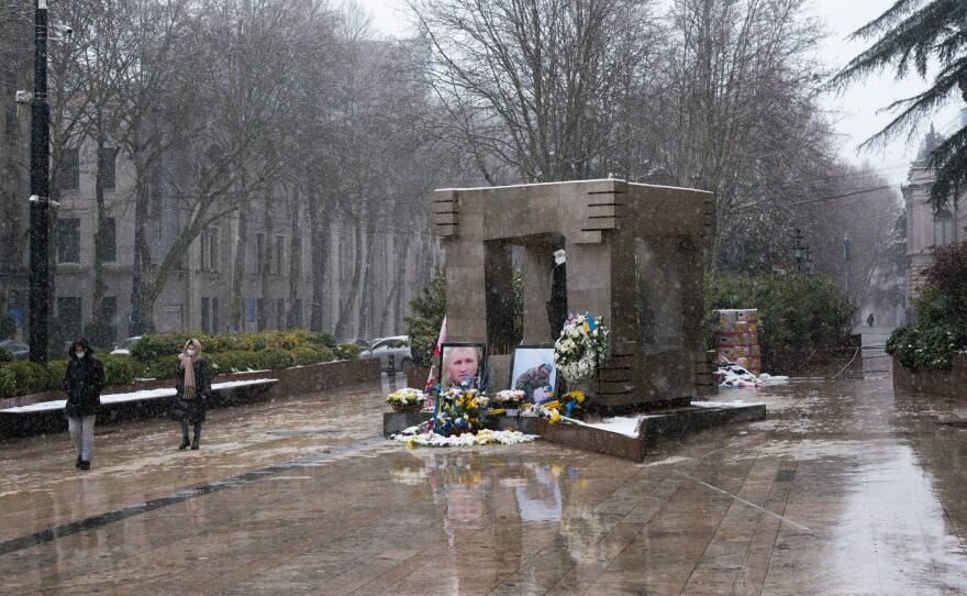 A memorial to Georgians who volunteered as soldiers and died in Ukraine sits outside Georgia's parliament building. The memorial of photos and flowers leans up against a permanent memorial for people who were killed in 1989 during an anti-Soviet protest that was crushed by the Soviet army.