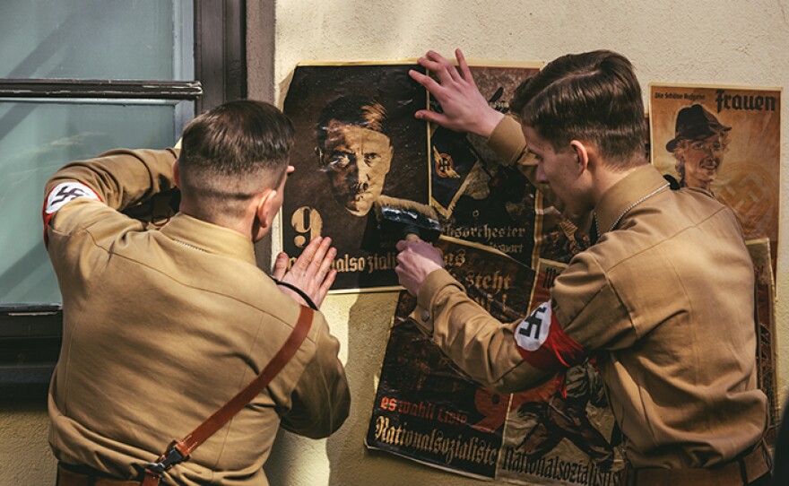 Drama reconstruction: Stormtroopers in uniforms post Hitler posters on wall.