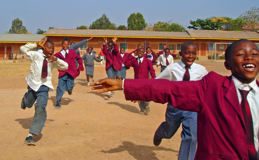 School children in Jos, Nigeria run across a field.