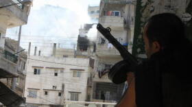Smoke billows from the Jabal Mohsen community while a Sunni gunman takes cover behind a wall in the Bab al-Tabbaneh neighborhood during clashes in Tripoli, Lebanon, on July 9, 2008.
