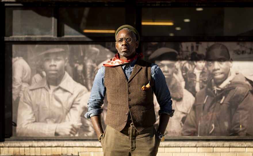 Attorney Kenneth Montgomery outside his office in Brooklyn's Crown Heights. In the window behind him, black boys in the 1980s pose for a photo by legendary street style photographer Jamel Shabazz.