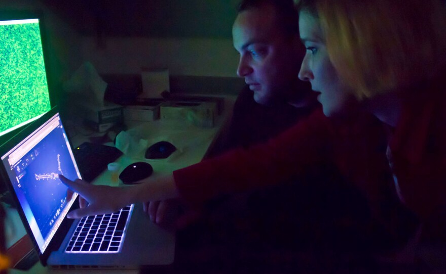Two EteRNA players check out a molecule designed using the online game. The display above shows output from a laser microscope that tests the new designs.