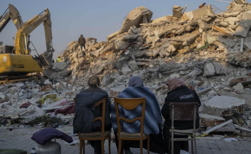 Women sit in front of the rubble of an area destroyed during the earthquake in Antakya, southeastern Turkey, Sunday, Feb. 12, 2023.