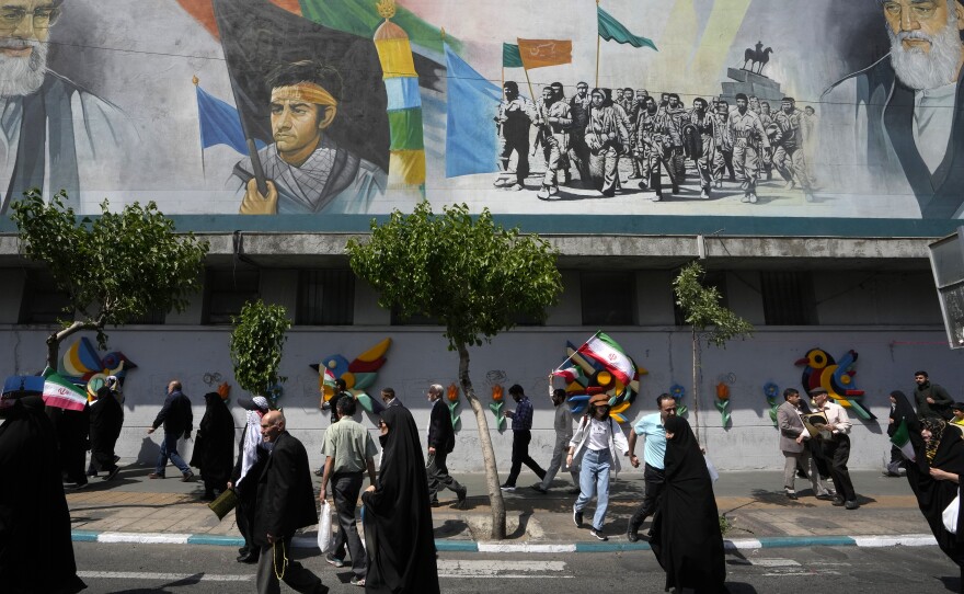 Iranian worshippers walk past a mural showing the late revolutionary founder Ayatollah Khomeini, right, Supreme Leader Ayatollah Ali Khamenei, left, and Basij paramilitary force, in an anti-Israeli gathering after their Friday prayer in Tehran, Iran, on Friday.
