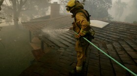 Firefighters Hollis Frands sprays down a rooftop to prevent it from catching on fire October 23, 2007 in Poway, California. The Witch Fire, which started outside of Ramona, California burned more than 1,000 structures and forced more than 300,00 to evacuate. (Editor's Note: KPBS initially posted a photo of the Harris Fire in this story, which is not at issue in this settlement. KPBS regrets the error.)