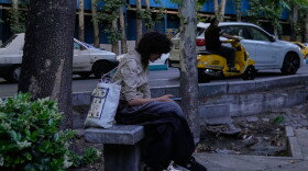 A woman checks her smartphone while sitting on a bench along a sidewalk in northern Tehran, Iran, Tuesday, May 26, 2026.