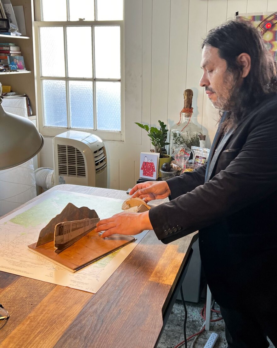 Artist Armando de la Torre is shown in an undated photo arranging a small-scale model of his forthcoming installation — a trolley, a mountain and an osprey catching a fish — at the Athenaeum Art Center in Logan Heights.