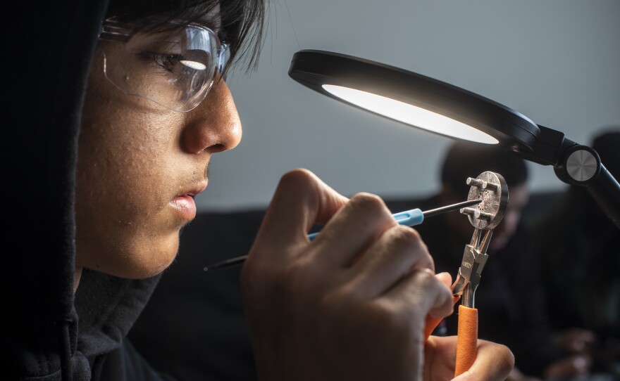 Kevin Mendoza, 15, a member of Team 8048 Churrobots of East Palo Alto, Calif., cleans dust particles off a gearbox component.