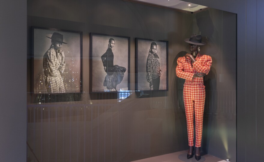 Chris Seydou's orange checkered suit and wide brimmed hat is ready to strut at the "Africa Fashion" show. The three photos of Seydou's clothes on the wall were made by Sierra Leone-born, London-based stylist IB Kamara, now editor-in-chief of the magazine <em>Dazed.</em>