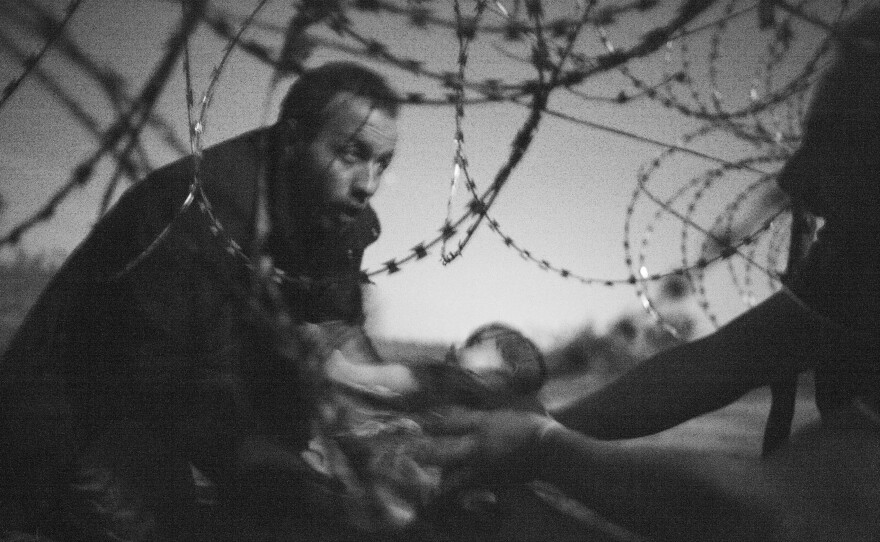 A man passes a baby through a barbed wire fence at the Serbia/Hungary border in Röszke, Hungary, on Aug. 28, 2015.