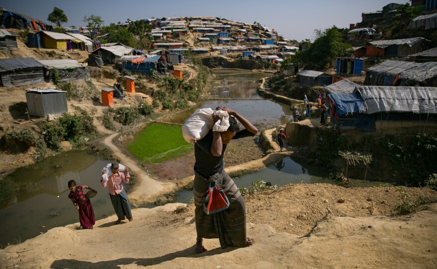 Mohamed Yonus (dark shirt, green skirt) carries his distribution bag to his home in the Hakimpara refugee camp.