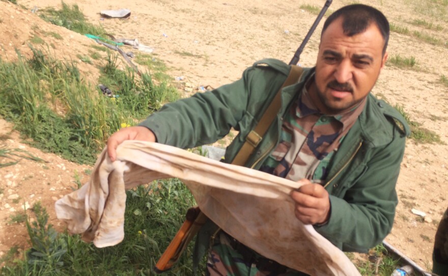 In August, the self-proclaimed Islamic State seized territory near the northern Iraqi village of Hardan. A handful of Yazidis who fled have returned to a grim discovery: mass burial pits. Here, Naif Brahem Khadir holds a traditional man's headdress with blood stains and a bullet hole. It was half-buried in a mound near the village. He believes his uncle and his cousin are among the bodies here.