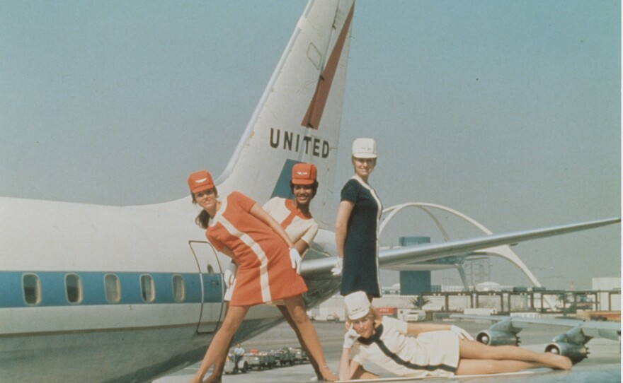 Four stewardesses posed on wing of airplane, circa 1965.