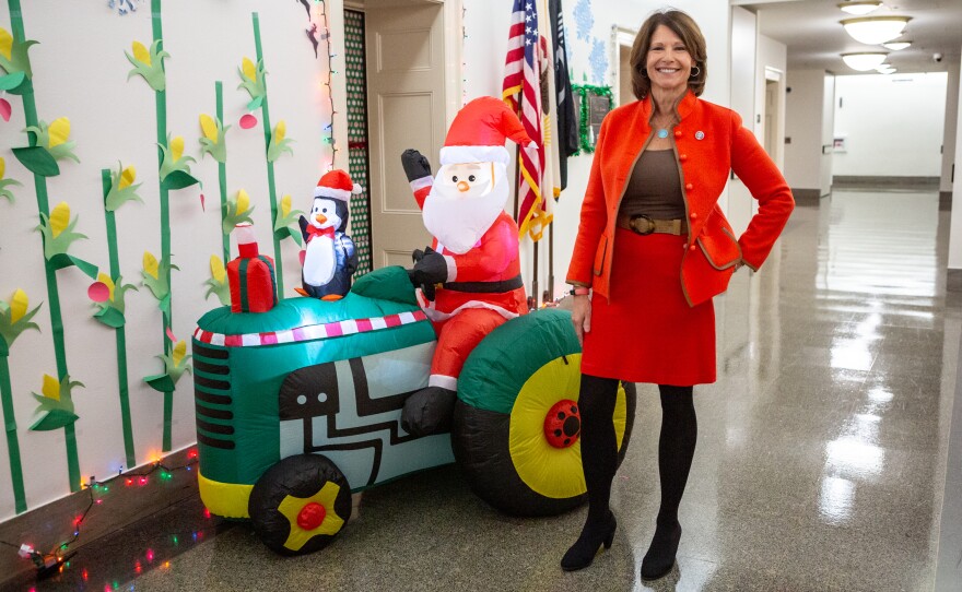 Democratic Rep. Cheri Bustos of Illinois stands next to her inflatable Santa driving a John Deere tractor outside of her office. The wall is adorned with paper cornstalks and snowflakes.