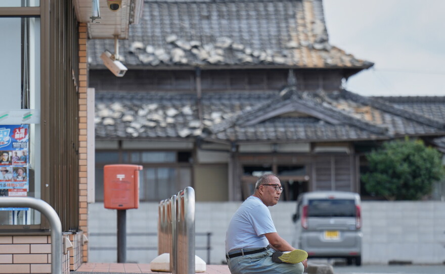 A person sits near a house damaged following an earthquake in Uki, Kumamoto Prefecture, southern Japan, Thursday, July 30, 2026.