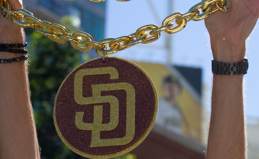 A Padres fan holds up a large "SD" pendant chain necklace outside Petco Park before game two of the NLCS on Oct. 19, 2022. 