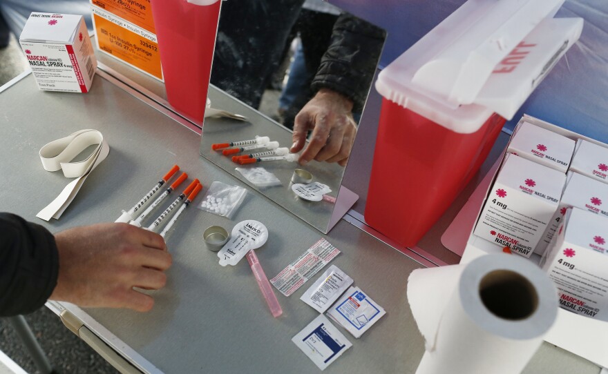 A visitor to the Harvard School of Public Health's mock safe injection site checks out the items on the demonstration table set up underneath a tent on the quad near the medical school in Boston on April 30, 2018.