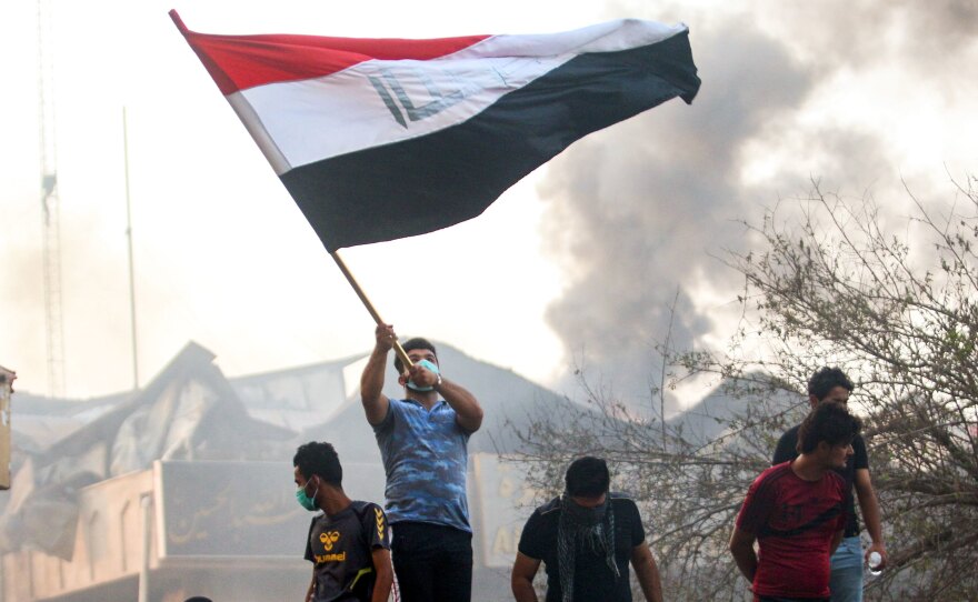 An Iraqi protester waves a national flag while demonstrating outside the burnt-down local government headquarters in the southern city of Basra on Sept. 7, during demonstrations over problems including poor public services.