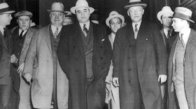Al Capone (front and center) being escorted to the train in Chicago that will take him to U. S. Federal Penitentiary in Atlanta. U. S. Marshal Laubenheimer is to his right and the car thief transported with him is between them in the second row. In the second row, far right with the white hat, is almost certainly Eliot Ness. He and the Untouchables were (as reported in the Chicago newspapers), guarding Capone until he was safely on the train to Atlanta.