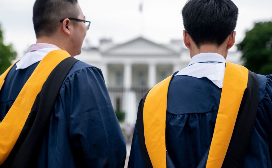 Students from George Washington University wear their graduation gowns outside of the White House in Washington, D.C, on May 18. Economists worry President Biden's plan to forgive student loans could encourage more people to take on debt in the hopes of also being forgiven.