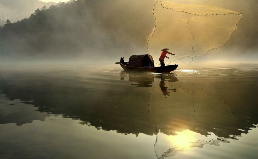 A fisherman throws out his net in the hazy morning light.