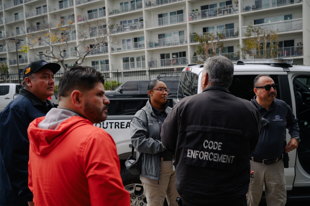 National City HOME team caseworkers Qiana Williamson, center, and Hector Hueso, far right, talk with city code enforcement officers near a tent where an unhoused resident was barbecuing in National City, California on March 7, 2024. National City is the second in San Diego County to move away from a police-led response to homelessness and toward trained caseworkers.