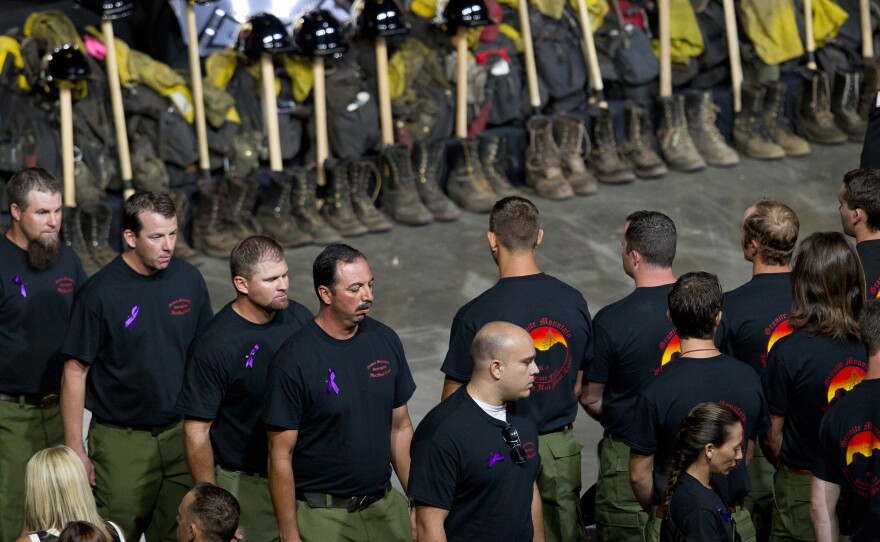 Former Granite Mountain Hotshot firefighters walk past ceremonial firefighter boots and clothing during a memorial service honoring 19 fallen firefighters in Prescott Valley, Ariz, Tuesday.