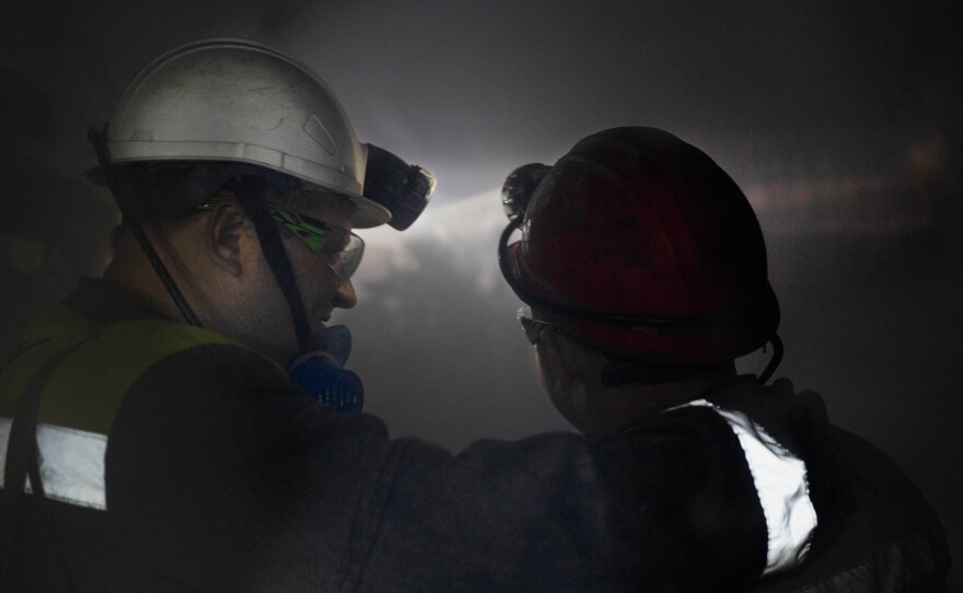 Mine workers are surrounded by dust as a drill bit chews into the wall of the mine.