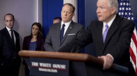 White House Senior Adviser Stephen Miller listens at left as Attorney General Jeff Sessions, right, accompanied by White House press secretary Sean Spicer, talks to the media during the daily press briefing at the White House in Washington, Monday, March 27, 2017. 