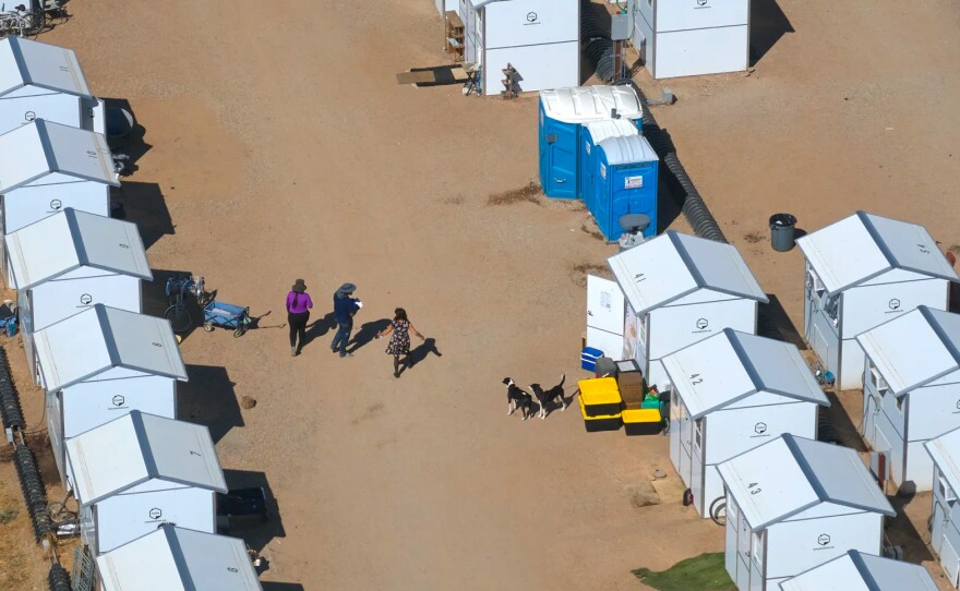 People and dogs walking between pallet shelters at an emergency non-congregate housing site in Chico on Sept. 6, 2023.