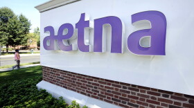 A pedestrian walks past a sign for Aetna Inc., at the company headquarters in Hartford, Conn., Aug. 19, 2014.