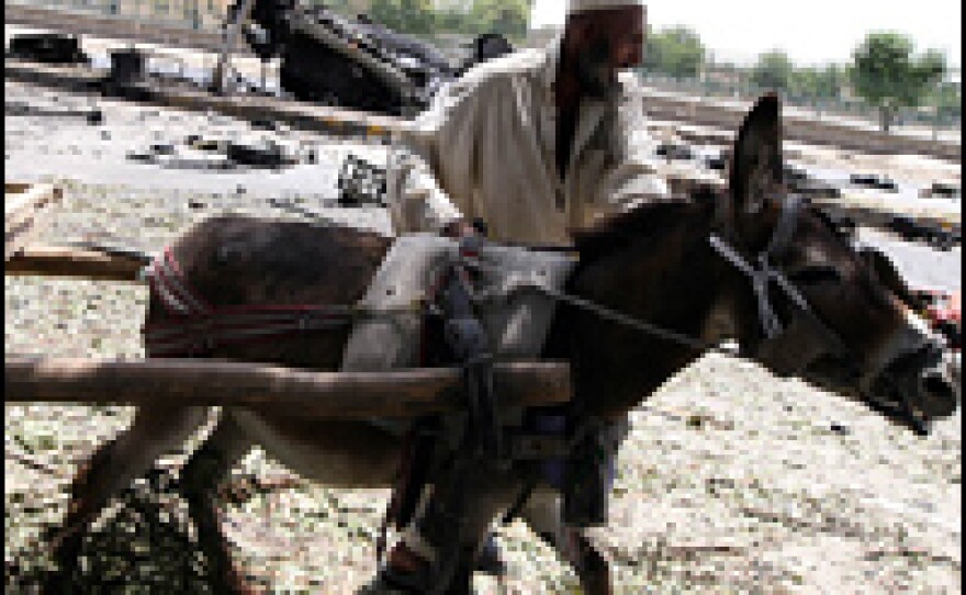 An Afghan farmer struggles with a donkey to pull a wooden cart past the wreckage of the demolished American armored vehicle.