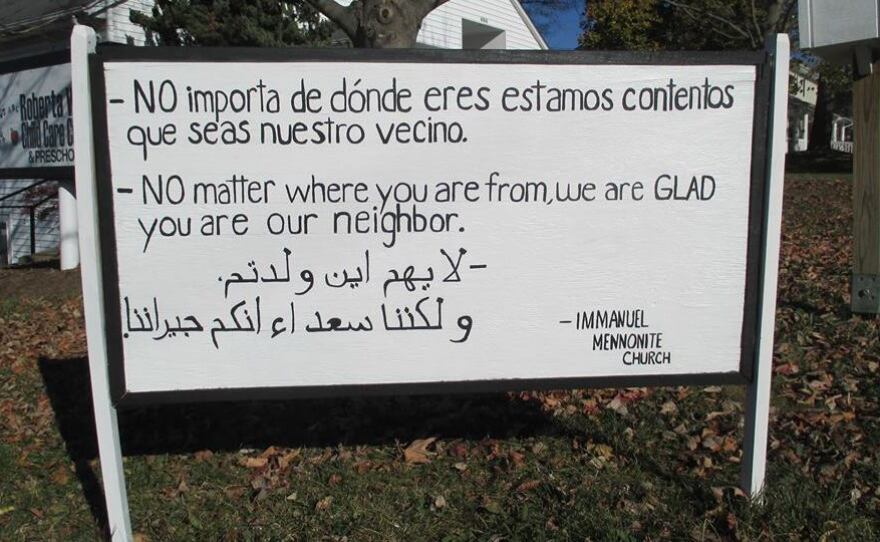 The original black-and-white wooden sign at Immanuel Mennonite in Harrisonburg, Va., has inspired thousands of yard signs. It was written by Pastor Matthew Bucher and translated with the help of congregation members and friends.
