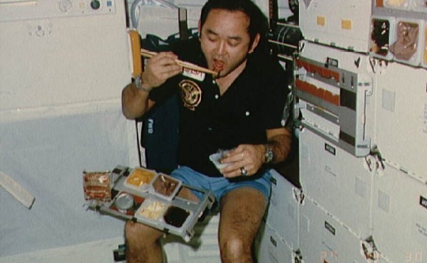 Mission specialist Ellison S. Onizuka takes a meal break on the mid-deck of the Discovery space shuttle during the STS 51-C mission in the 1980s.