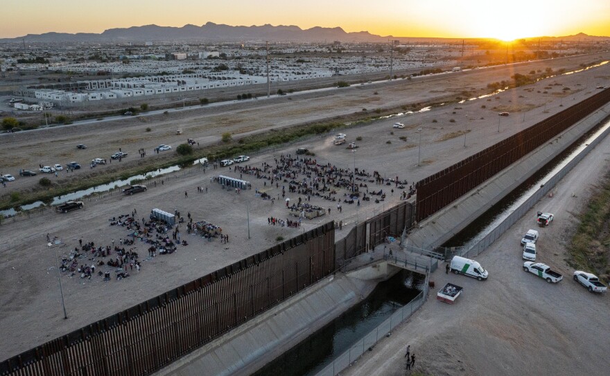 As the sun sets, migrants wait outside a gate in the border fence to enter into El Paso, Texas, to be processed by the Border Patrol, on Thursday.