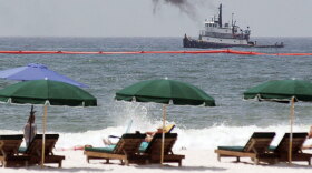 A tugboat works to lay boom in the Gulf of Mexico near Perdido Pass at Orange Beach, Ala., while beachgoers watch. Thousands of tourists will be changing vacation plans this summer because of the Gulf oil spill.