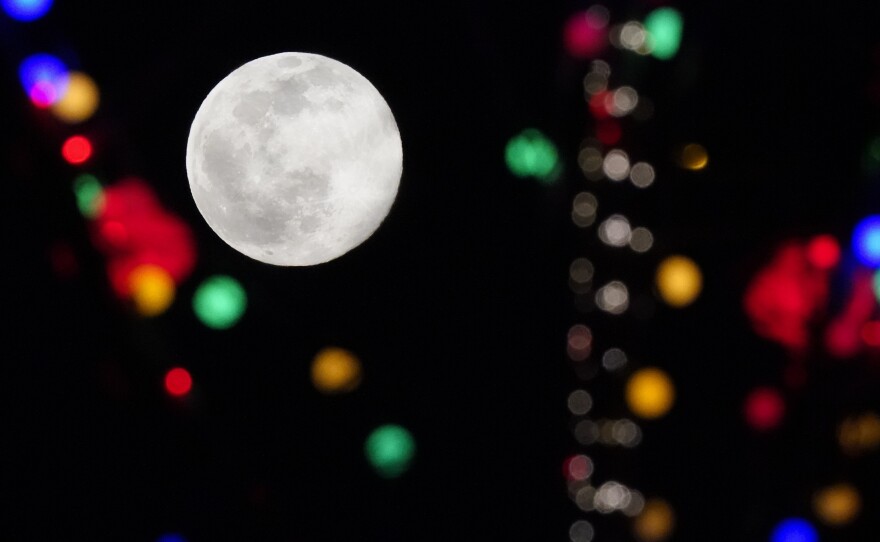 The full moon rises above strings of lights at the Olympic Green during the 2022 Winter Olympics on Wednesday in Beijing.