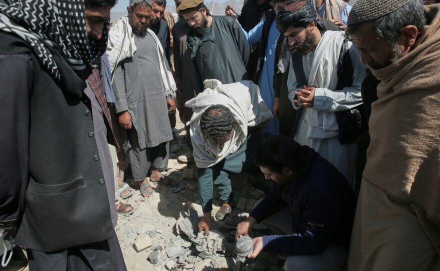 Residents and Taliban police gather the remains of a projectile at the site of a strike in Kabul, Afghanistan, on March 13.