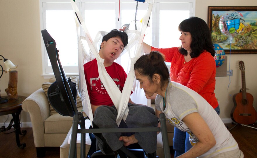 Justin Lee is loaded into a "stander" by his mother Judy, upper right, and his physical therapist, Rika Matsudo. The device allows Justin to be positioned upright for physical therapy.