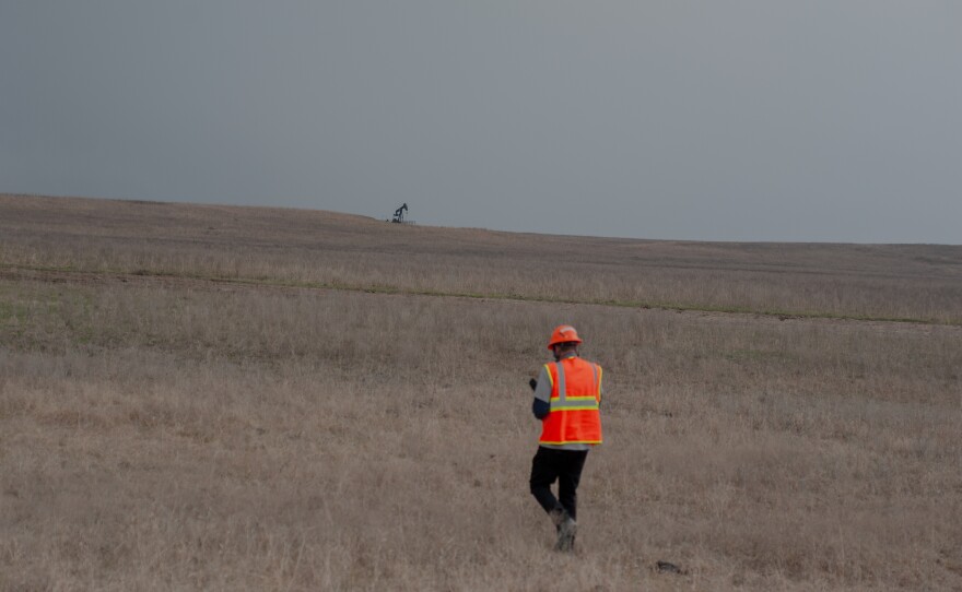 Caldwell walks through dry grass in the Tallgrass Prairie Preserve in Oklahoma on March 20, 2024. A pumpjack is visible in the distance.