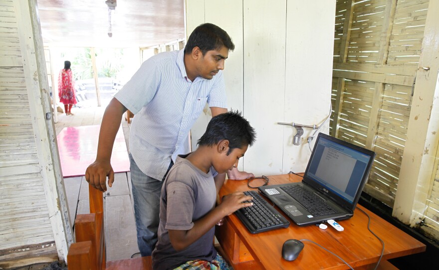 Mohammad Saiful Islam coaches a kid how to use a computer in a floating library run by the nonprofit group Shidhulai Swanirvar Sangstha.