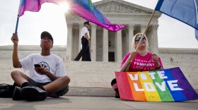 Carlos McKnight, 17, of Washington, left, and Katherine Nicole Struck, 25, of Frederick, Md., hold flags in support of gay marriage as security walks behind outside of the Supreme Court in Washington,  June 26, 2015. 