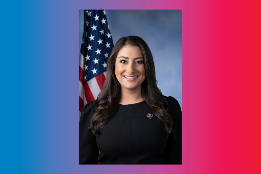 Headshot of San Diego Representative Sara Jacobs in a black top with an American flag on a flagpole visible over her right shoulder.