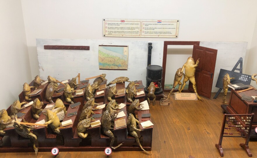 A Froggyland diorama shows a teacher trying to control a class in which students are hitting each other with rulers, arriving late to class and balancing pencils on their noses. Each  diorama displays anthropomorphized frogs in human scenes of the early 20th century.