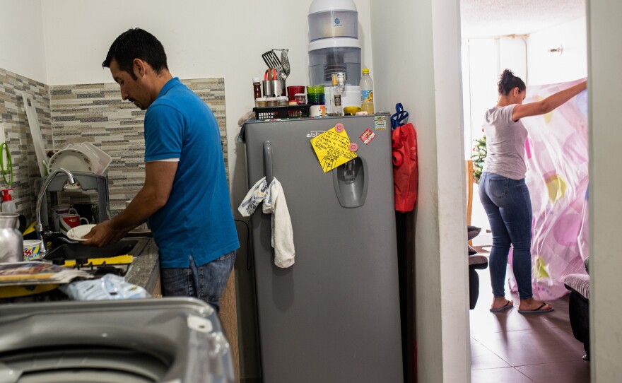 Ferley Sáenz and his wife, María Alejandra López, now divide up household chores. Here, Sáenz washes the dishes while López tidies up the living room.